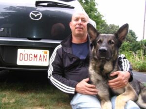Man and German Shepard Sitting Next to Car with Dogman License Plate